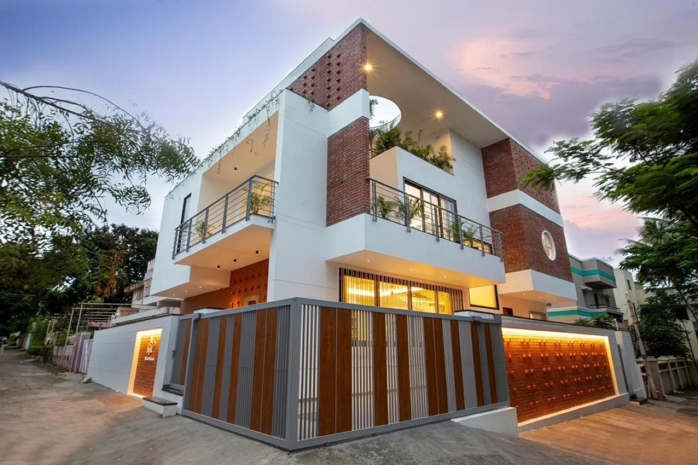 Modern two-storey house with red brick cladding on white exterior walls, featuring contemporary architectural design, balconies, and warm evening lighting.