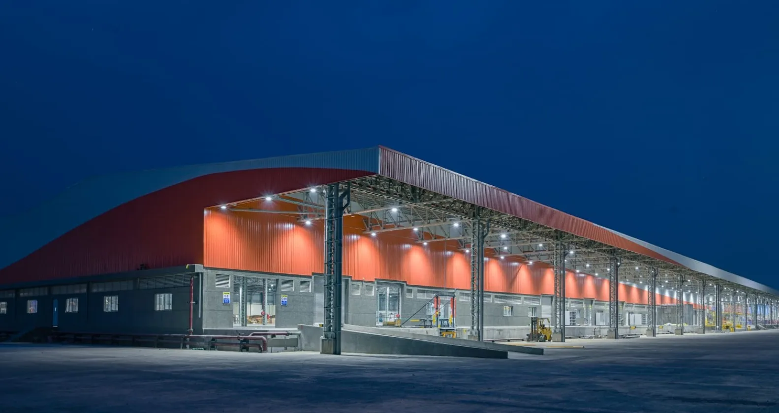 Modern industrial warehouse with steel roofing structure and illuminated factory exterior at night.