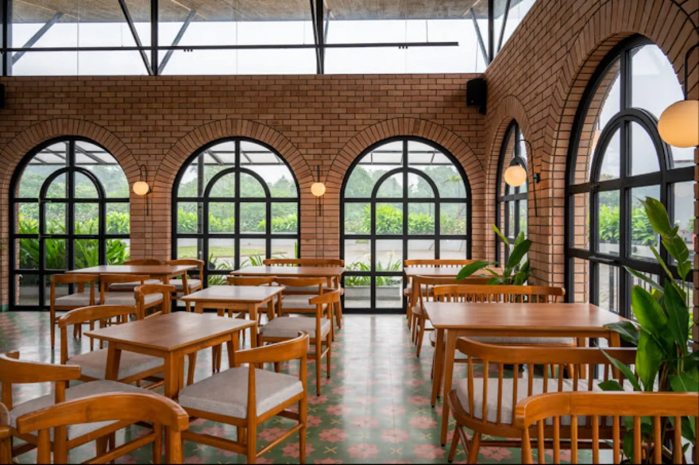 Modern restaurant interior featuring exposed red brick cladding walls, arched black-framed windows, wooden dining tables, and warm pendant lighting.